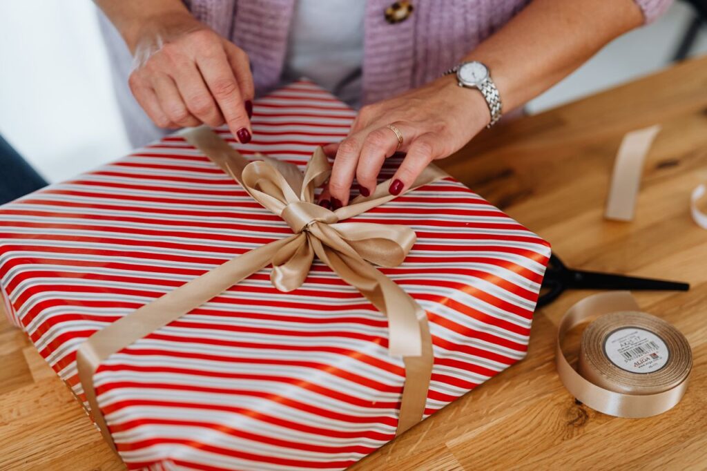 Close-up of adult wrapping a striped gift box with ribbon for Christmas celebration.